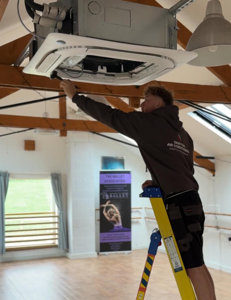 air conditioning engineer on step ladders cleaning an air conditioning unit